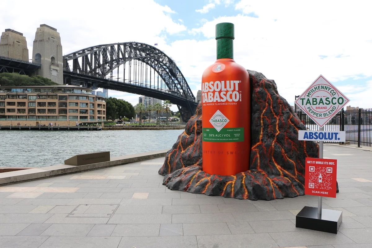 Activación OOH de ABSOLUT TABASCO en Sydney Harbour con una botella gigante emergiendo de un volcán frente al Harbour Bridge.