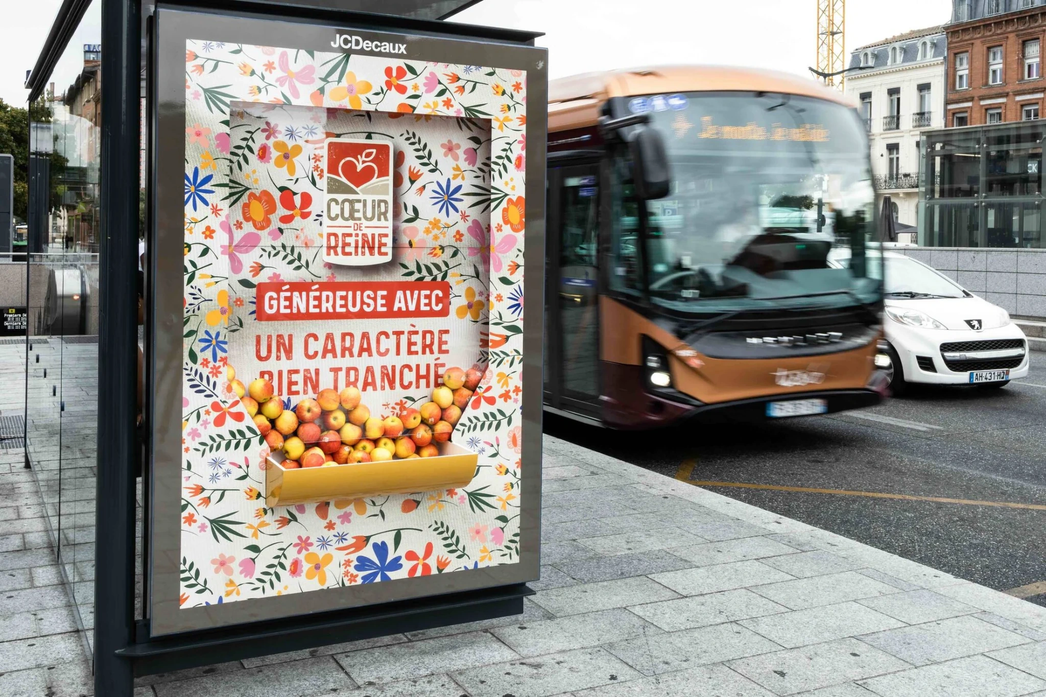 Publicidad Cœur de Reine en un paradero JCDecaux decorado con flores y un compartimento lleno de manzanas disponible para los peatones.