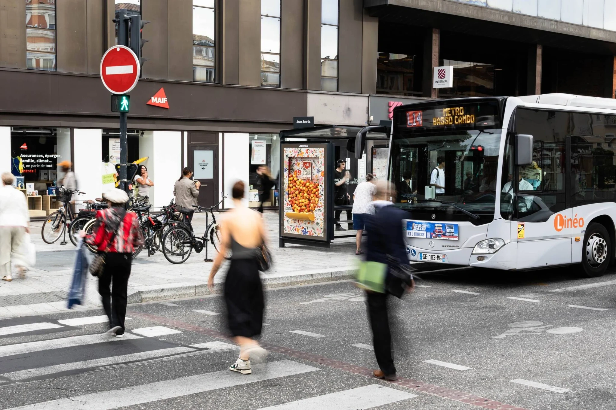 Paradero JCDecaux de Cœur de Reine con un dispensador de manzanas integrado al anuncio y peatones circulando junto al soporte.