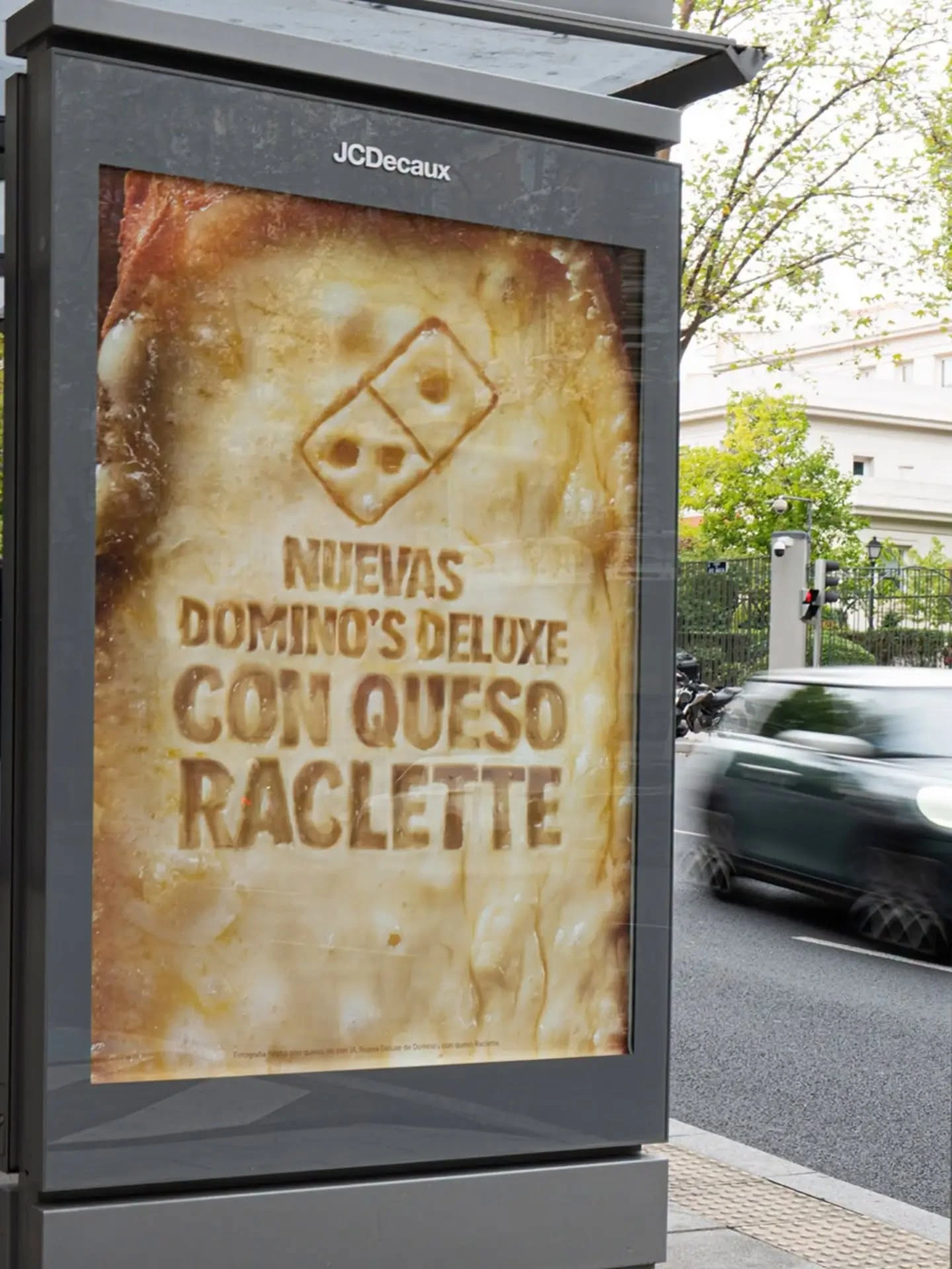 Mobiliario urbano de Domino’s con la campaña Nuevas Domino’s Deluxe con queso Raclette, utilizando una textura de queso real como fondo.