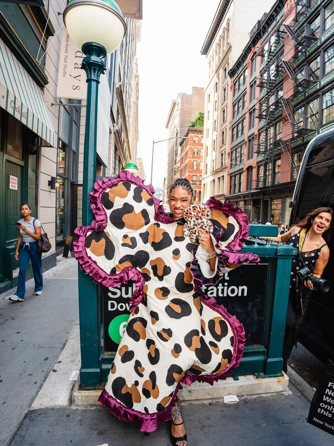 Modelo con un look de gran tamaño inspirado en alta costura y animal print sosteniendo un peluche Fuggler junto a una entrada del metro de Nueva York en SoHo.