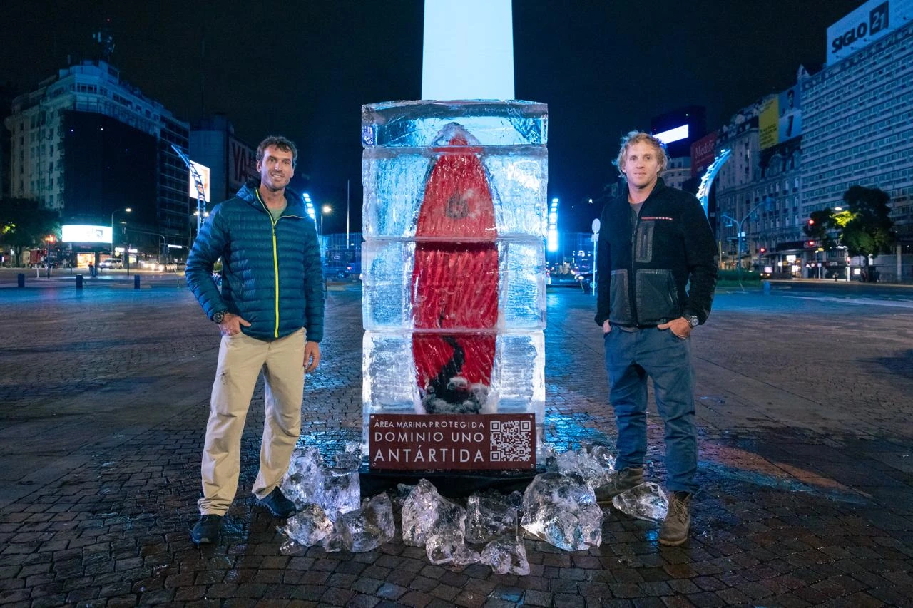 Joaquín y Julián Azulay junto a una tabla de surf congelada en un bloque de hielo frente al Obelisco de Buenos Aires para la campaña Antártica - Dominio Uno.