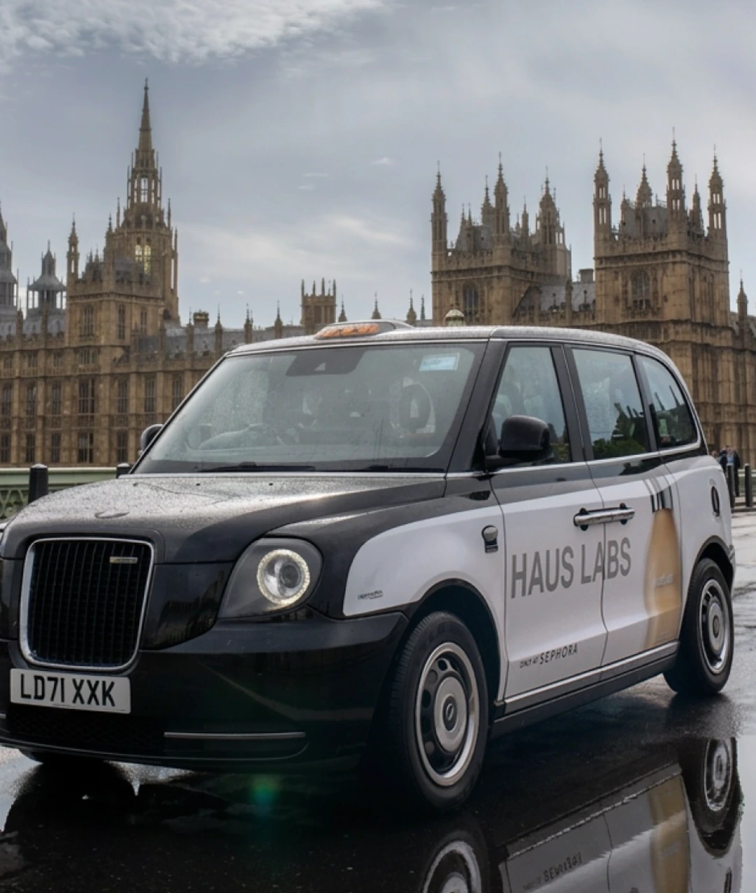 Taxi negro en Londres rotulado con Haus Labs frente al Palacio de Westminster como parte de la campaña For sexy skin.