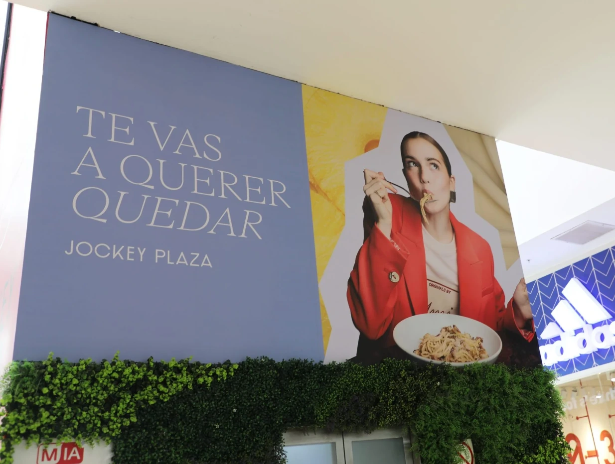 Campaña interior de Jockey Plaza con una mujer comiendo y el mensaje Te vas a querer quedar en una superficie de gran formato.