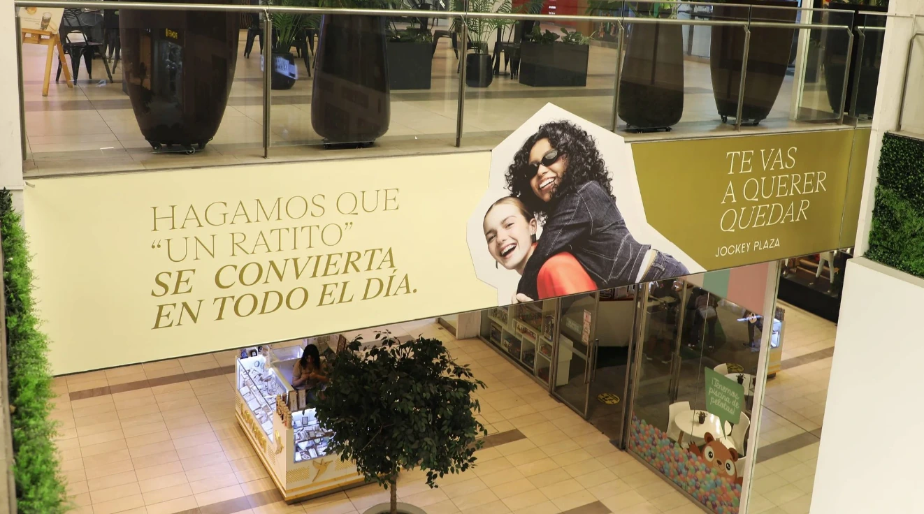 Campaña de Jockey Plaza dentro del centro comercial con el mensaje Hagamos que un ratito se convierta en todo el día y la firma Te vas a querer quedar.