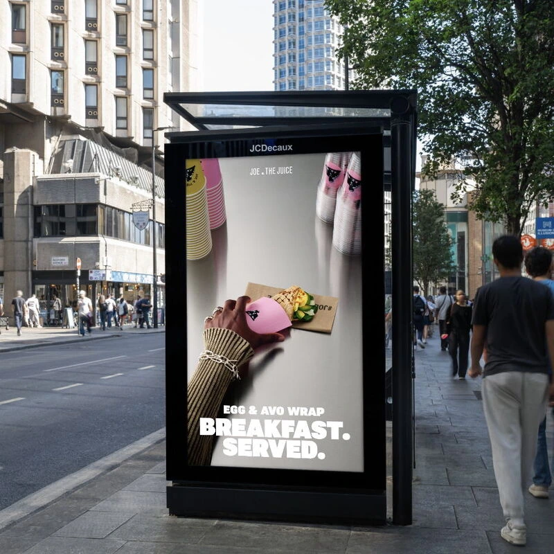Pantalla digital de JOE & THE JUICE en Londres mostrando el Egg & Avo Wrap con el mensaje Breakfast. Served. en mobiliario urbano JCDecaux.