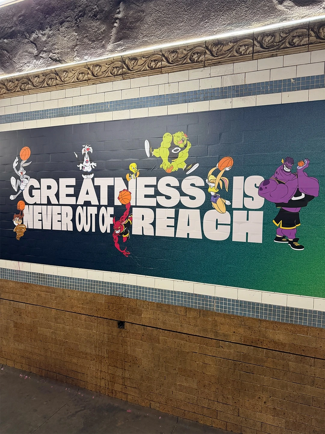 Mural en el subway de Nueva York con personajes animados de Space Jam jugando basketball alrededor del mensaje Greatness Is Never Out of Reach.