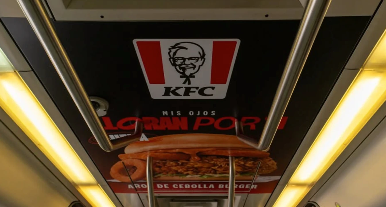 Publicidad de KFC Colombia para la Aros de Cebolla Burger instalada en el techo interior de un vagón.