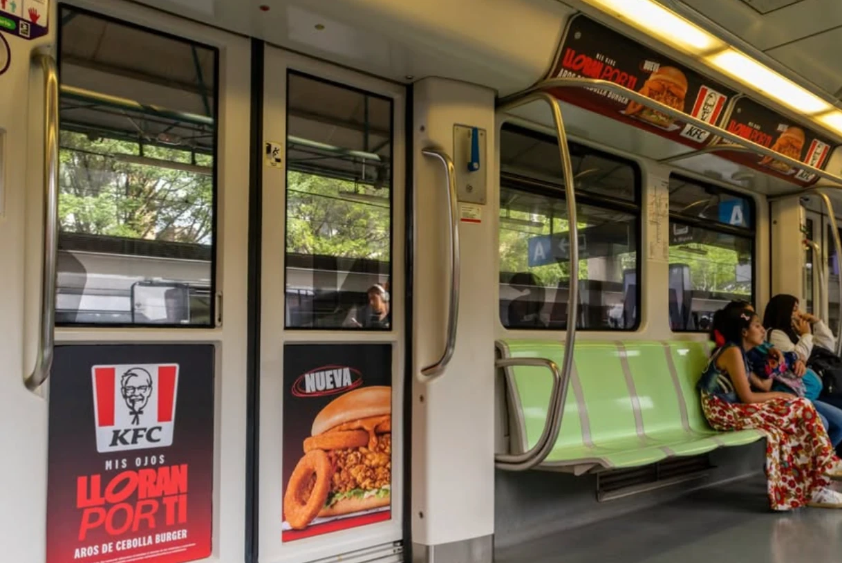 Paneles y puertas interiores de un tren con publicidad de KFC Colombia para la Aros de Cebolla Burger.
