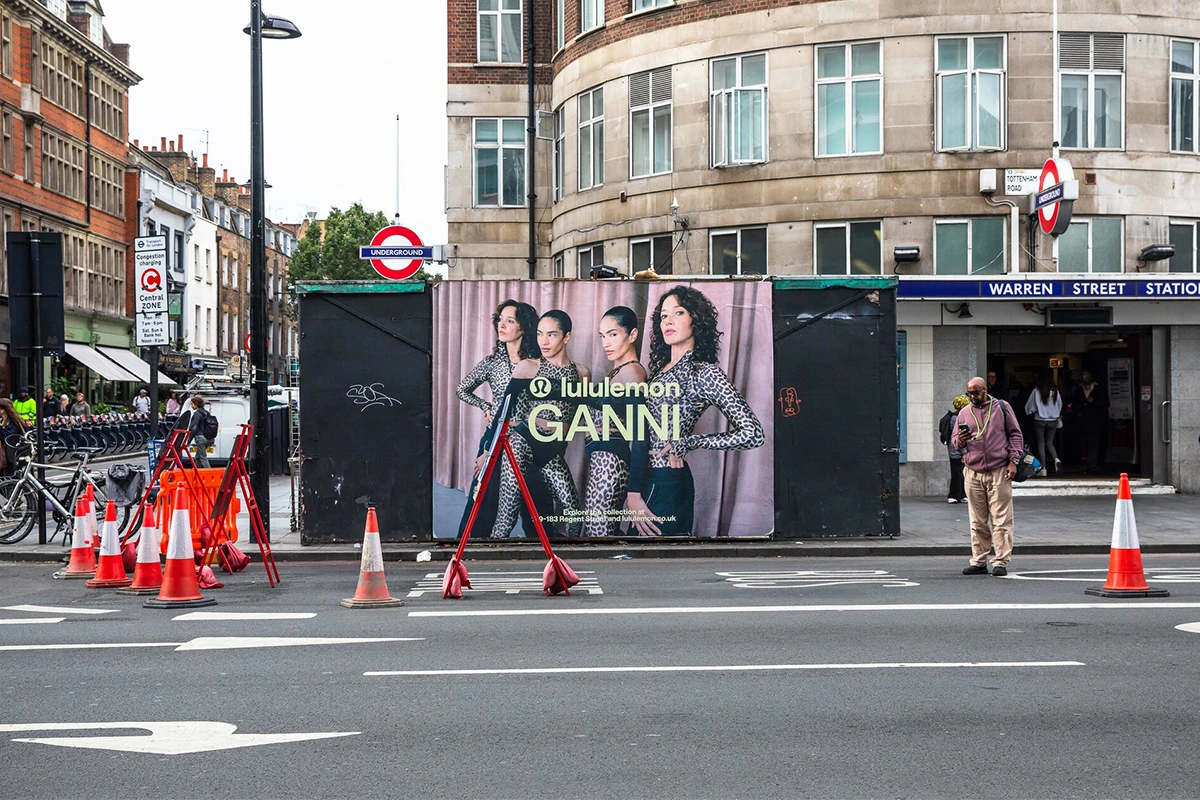 Poster exterior de la colaboración Lululemon x GANNI frente a Warren Street Station en Londres, mostrando modelos con activewear estampado.
