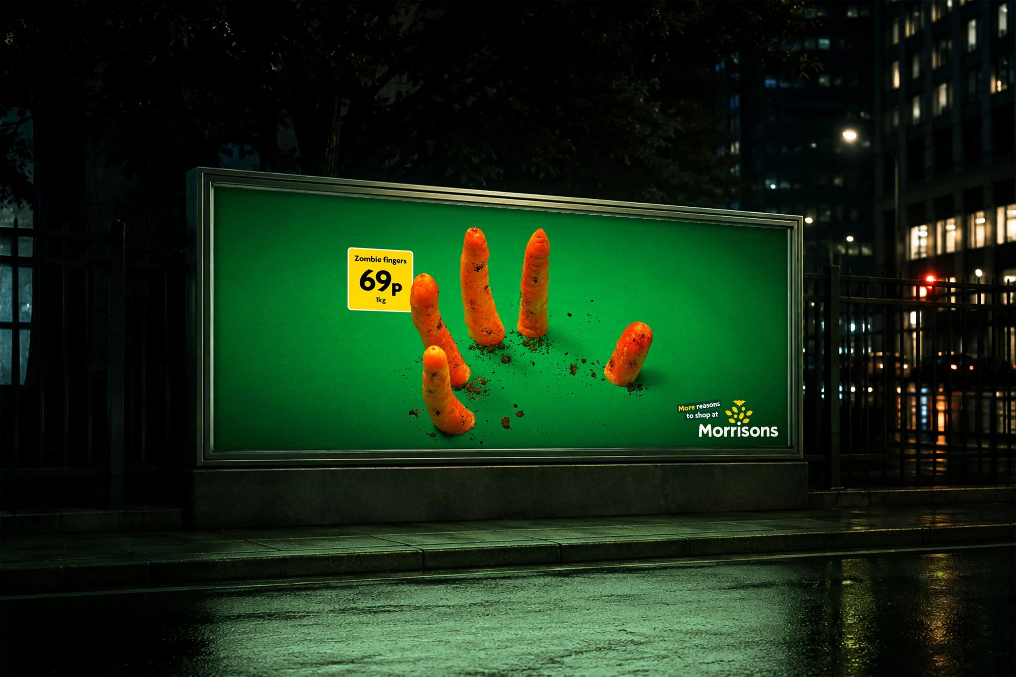 Billboard nocturno de Morrisons con zanahorias saliendo de la tierra como dedos de zombie y el precio 69p por kilo.