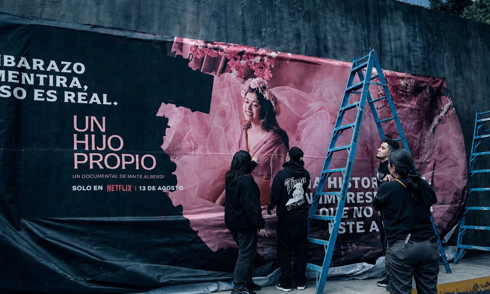 Billboard de Netflix para Un hijo propio extendido sobre un muro mediante una gran superficie textil rosa y negra que sale del marco publicitario.
