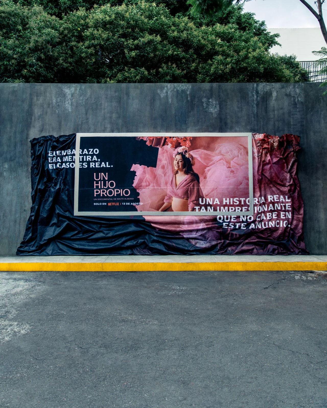 Campaña OOH de Netflix para Un hijo propio con una tela rosa y negra que sale del marco del anuncio y se extiende sobre el muro.