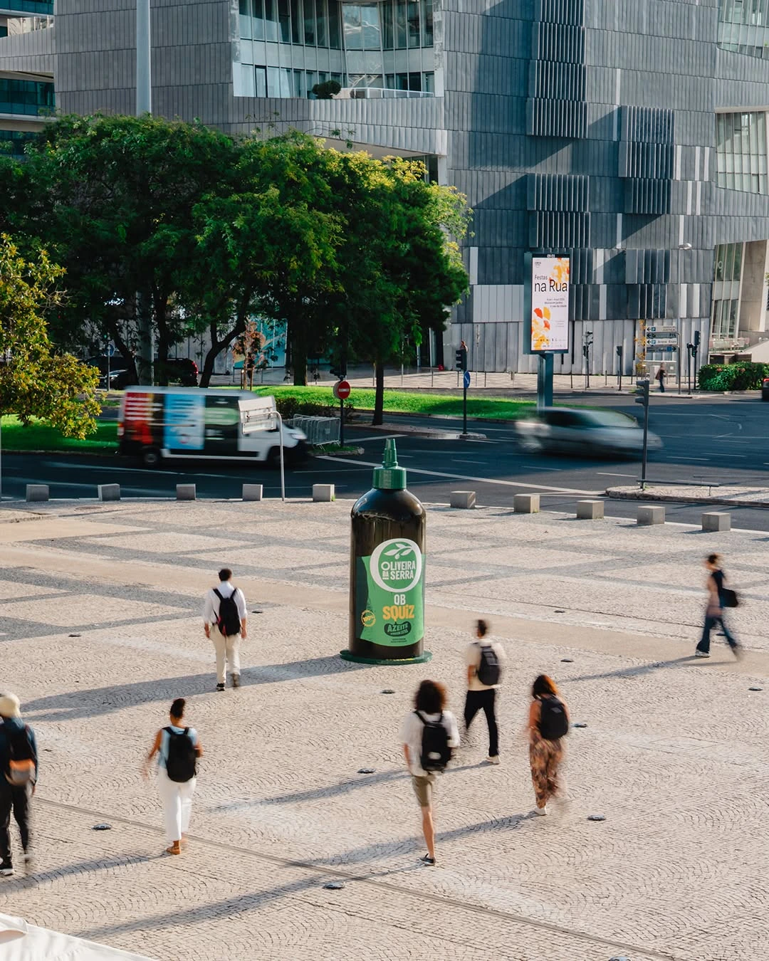 Botella XXL de Oliveira da Serra rodeada por peatones en una plaza urbana de Lisboa.