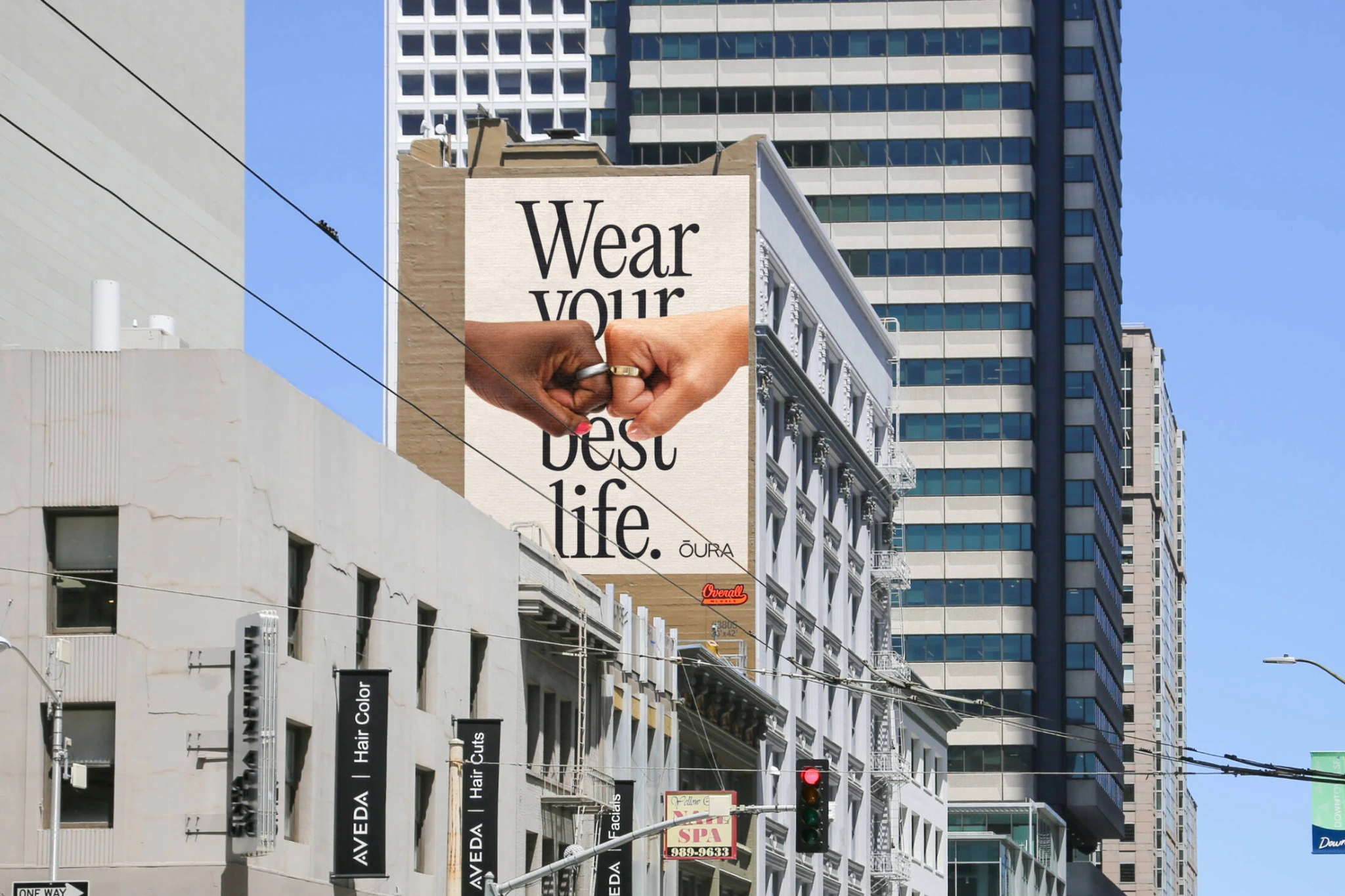 Billboard vertical de Oura en una zona urbana con dos manos usando anillos y el mensaje Wear your best life.