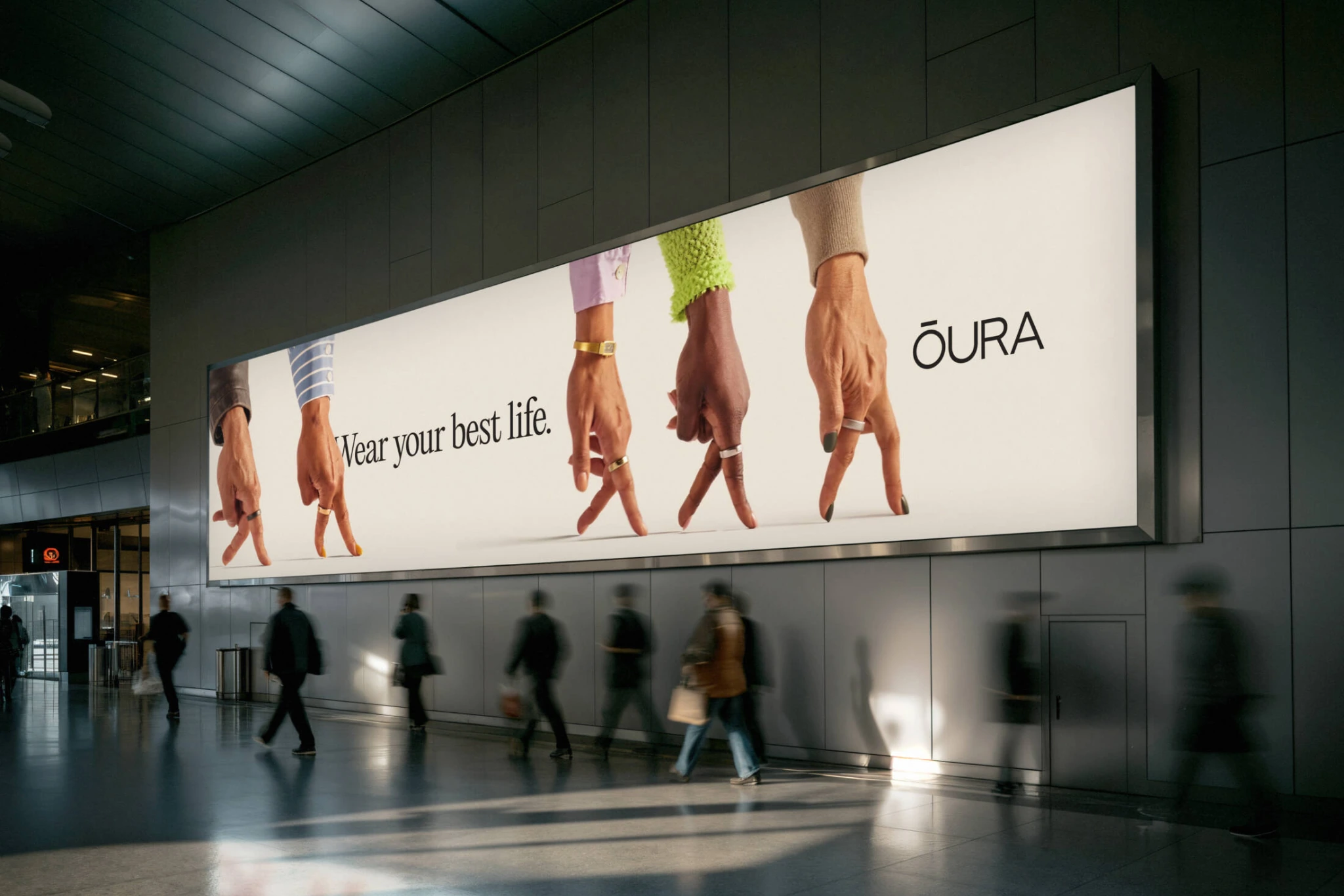 Billboard horizontal de Oura en un espacio de tránsito con varias manos caminando sobre sus dedos y el mensaje Wear your best life.
