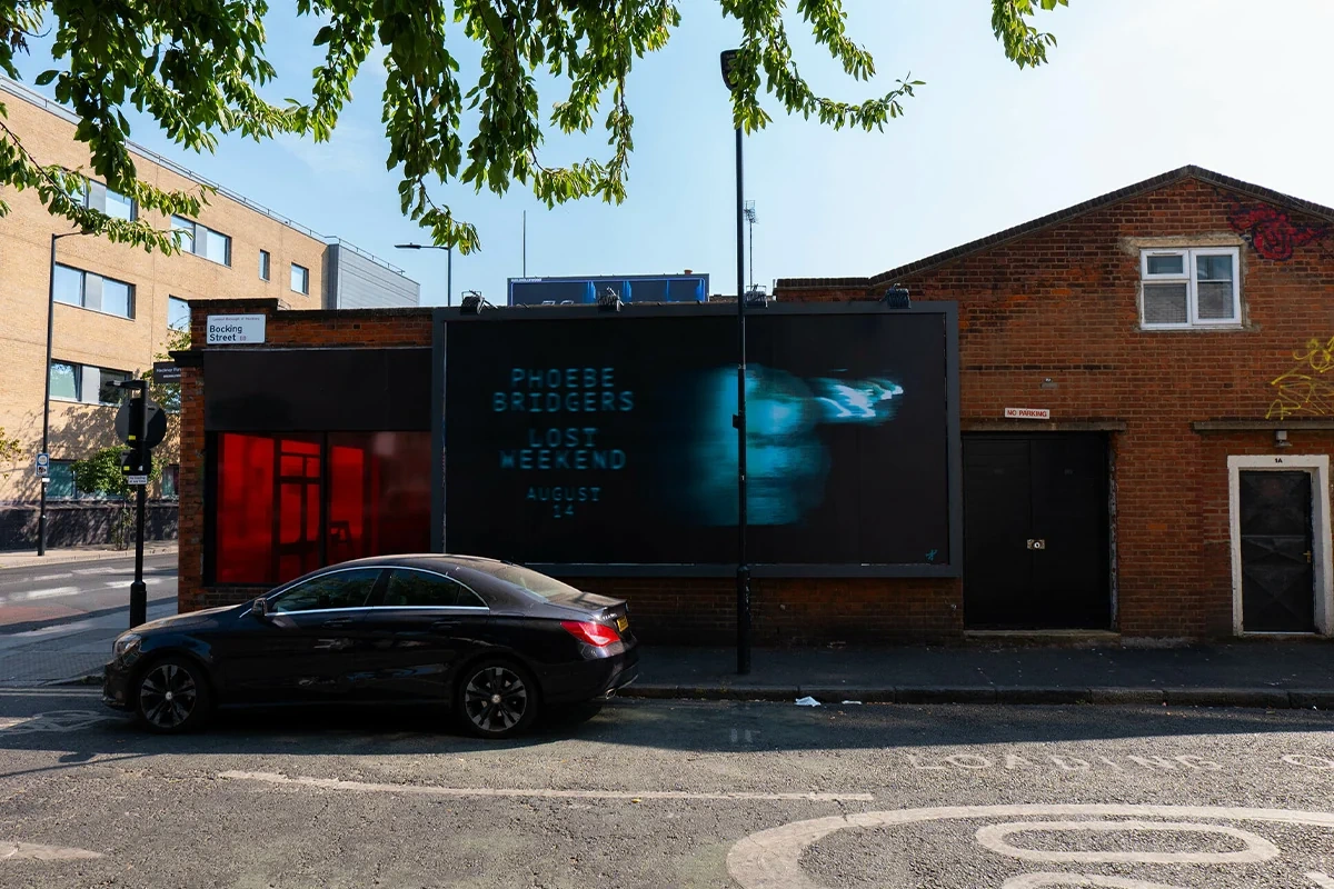 Billboard de Phoebe Bridgers para Lost Weekend en Mare Street con tipografía azul y una imagen distorsionada sobre fondo oscuro.