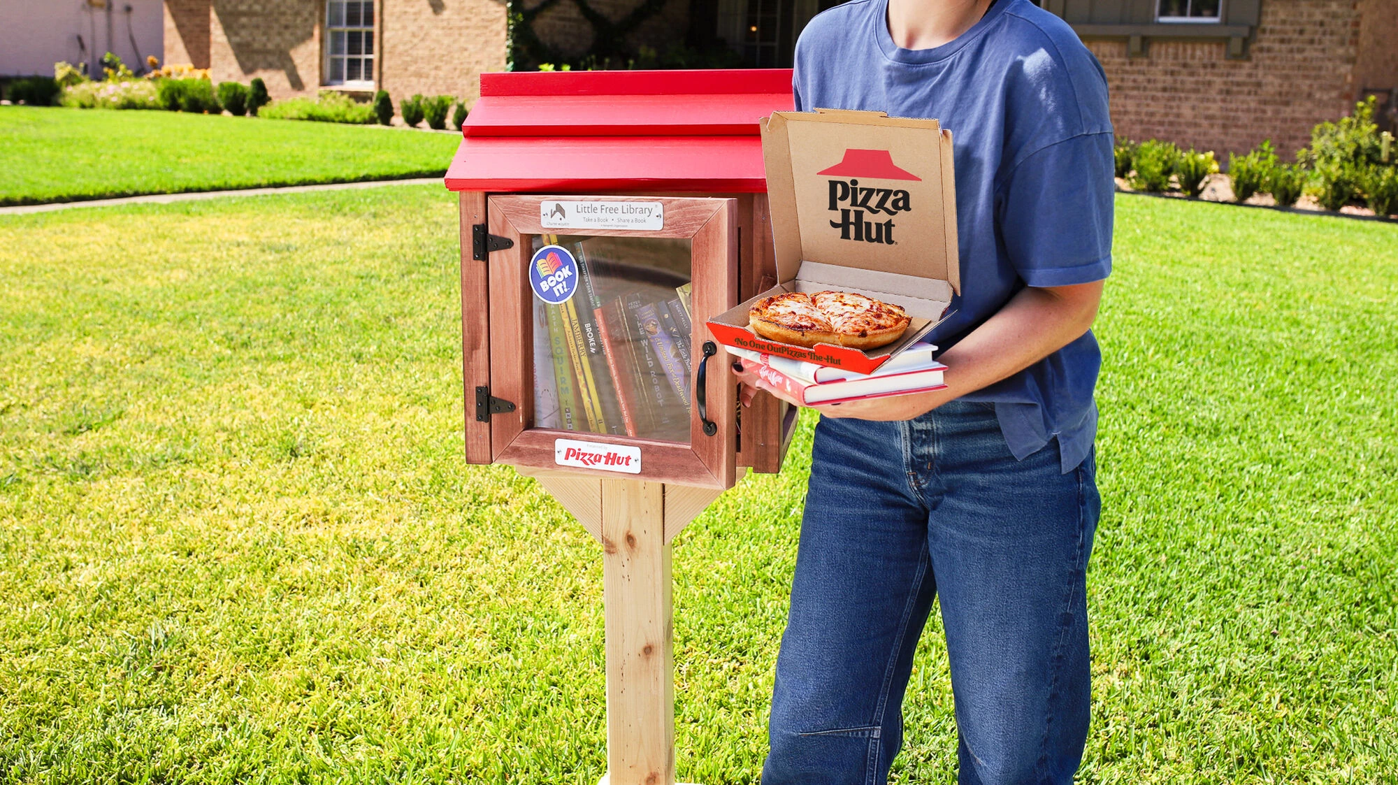 Persona sosteniendo una Little Hut Library de Pizza Hut con libros y una Personal Pan Pizza en una caja abierta.