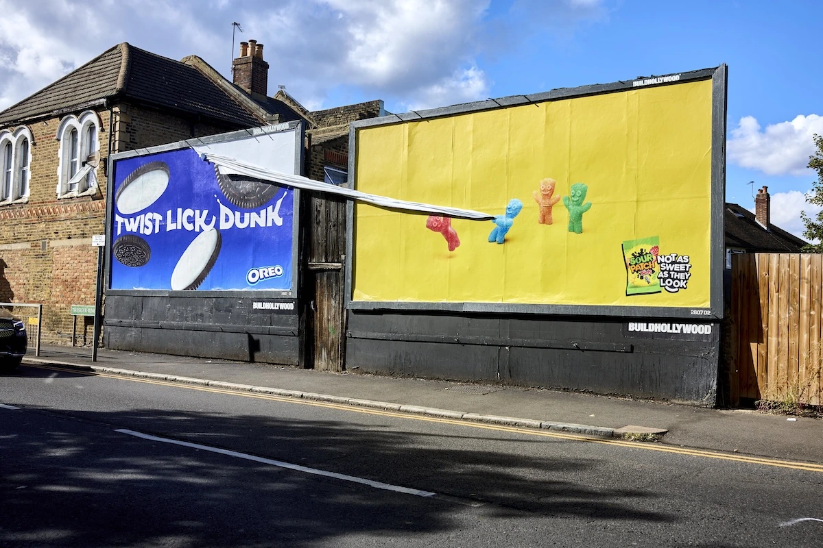 Ejecución special-build de Sour Patch Kids junto a un anuncio de Oreo, donde una estructura conecta ambas piezas y parece intervenir físicamente el billboard vecino.