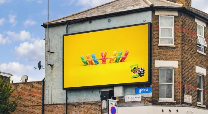 Billboard de Sour Patch Kids con personajes tirando de otro en una dinámica visual tipo tug of war sobre fondo amarillo.