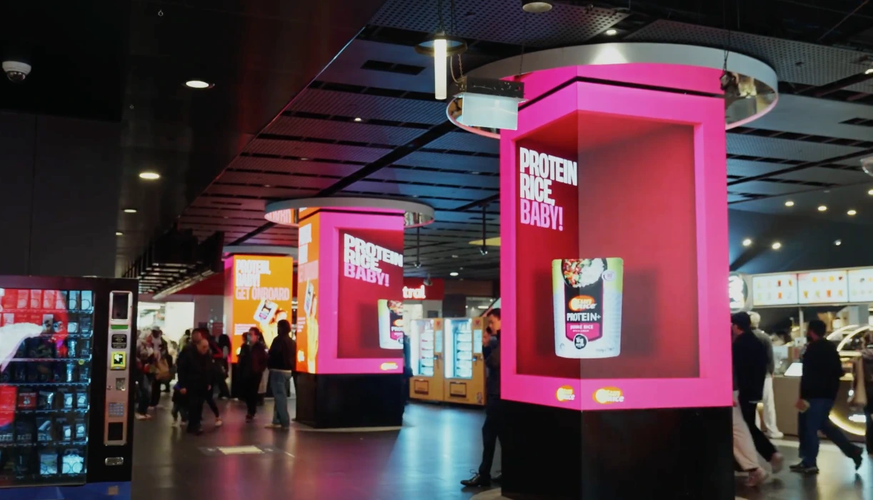 Columnas intervenidas con la campaña SunRice Protein Rice Baby y empaques Microwave Protein+ en un espacio interior de alto tráfico.