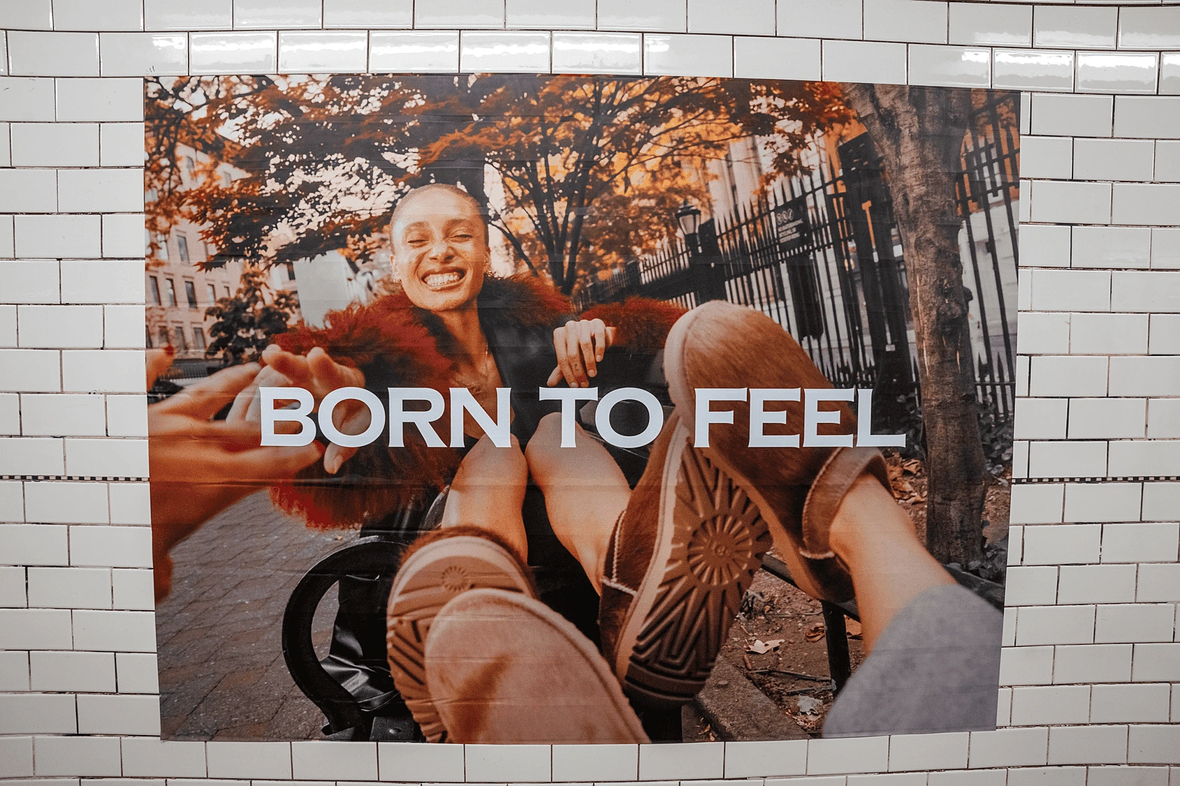 Publicidad de UGG Born To Feel en el subway de Nueva York con botas en primer plano y el mensaje Born To Feel sobre azulejos blancos.