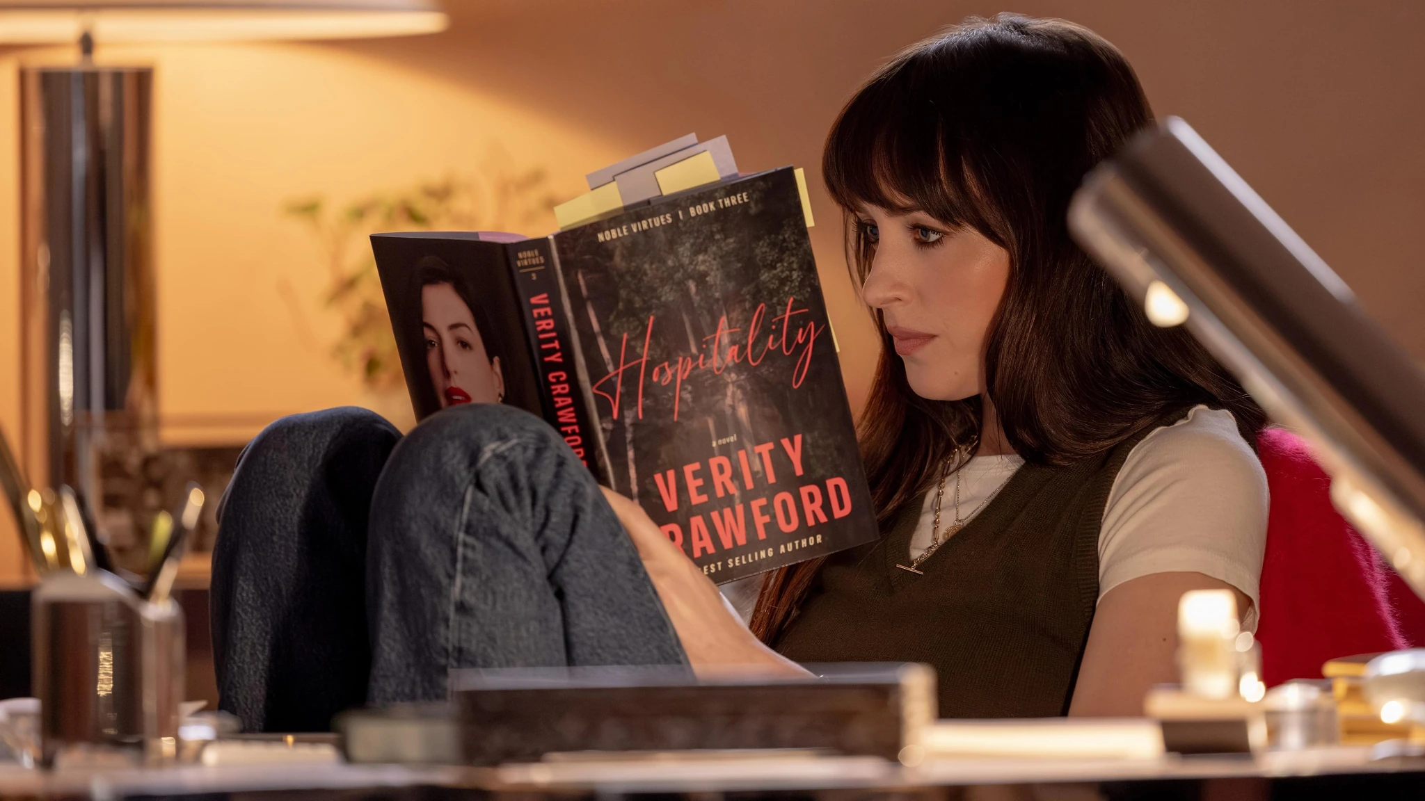 Escena promocional de Verity con una mujer leyendo un ejemplar del libro Hospitality dentro de un espacio interior.
