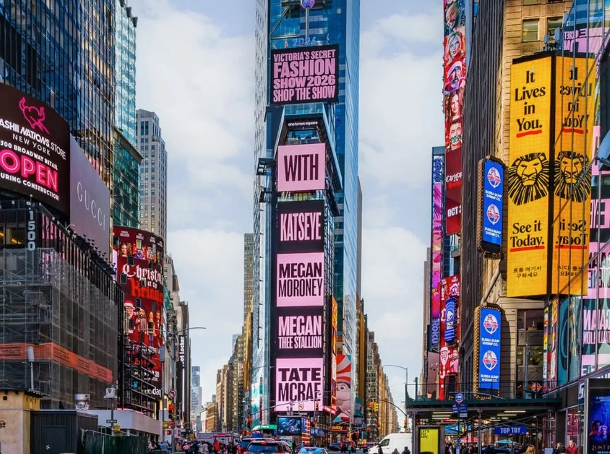 Toma de One Times Square con el anuncio de Victoria’s Secret Fashion Show 2026 y nombres de artistas en paneles rosas.
