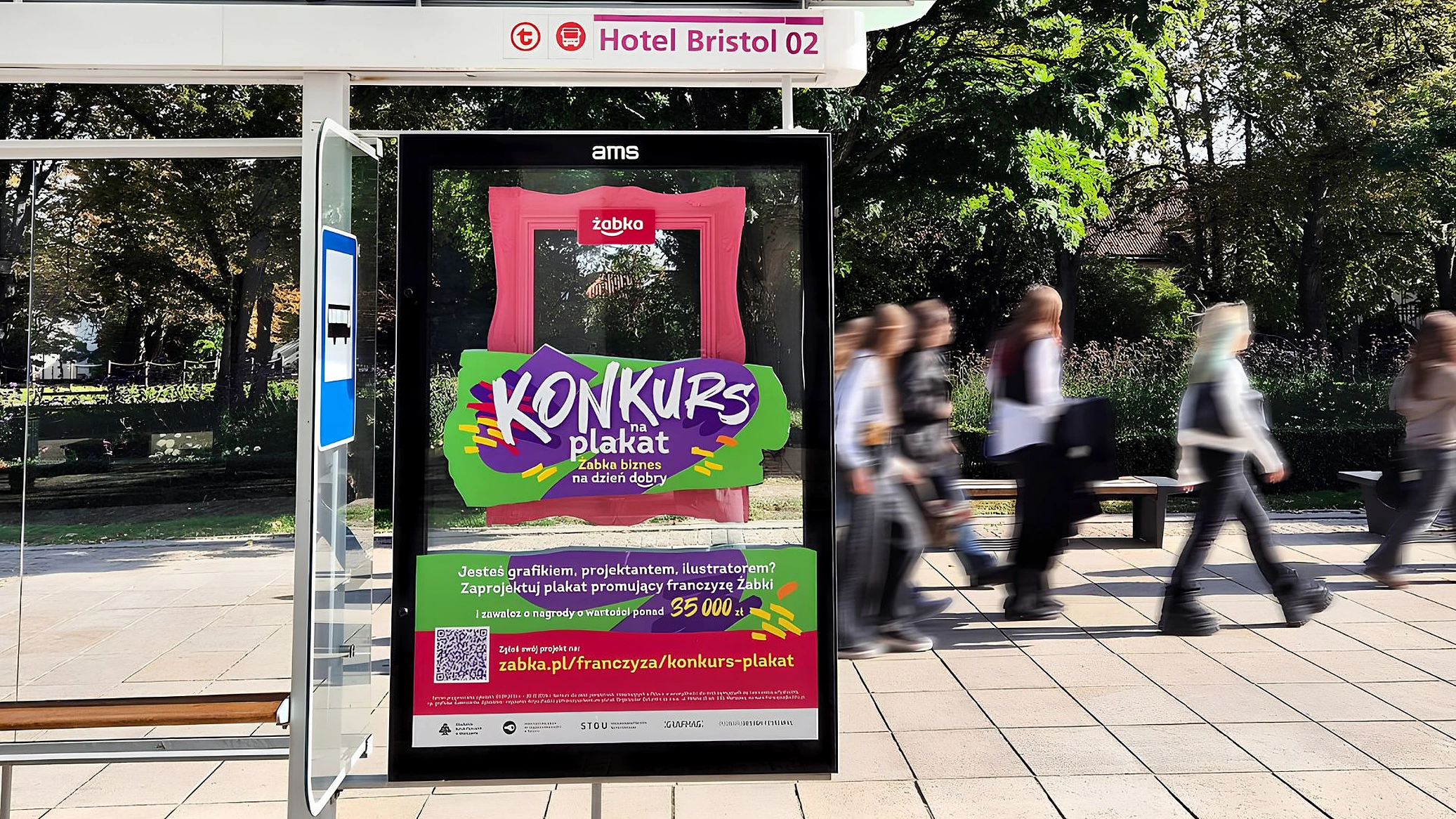 Paradero publicitario de Żabka en Polonia con un marco rosa tridimensional, gráficos del concurso de carteles, código QR y peatones pasando frente al soporte.